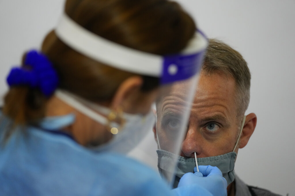 Charles Hoppmann is swabbed for a COVID-19 test as his family of four departs for a vacation in Milan, Italy, at a testing center operated by Nomi Health inside Miami International Airport, Friday, Dec. 17, 2021, in Miami. Nomi nurses said that both demand for tests and positivity rates at their testing center have risen significantly since Thanksgiving. (AP Photo/Rebecca Blackwell)